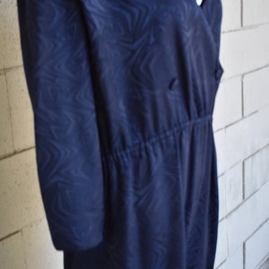 May include: A navy blue dress with a swirling pattern. The dress has a V-neckline and a cinched waist.