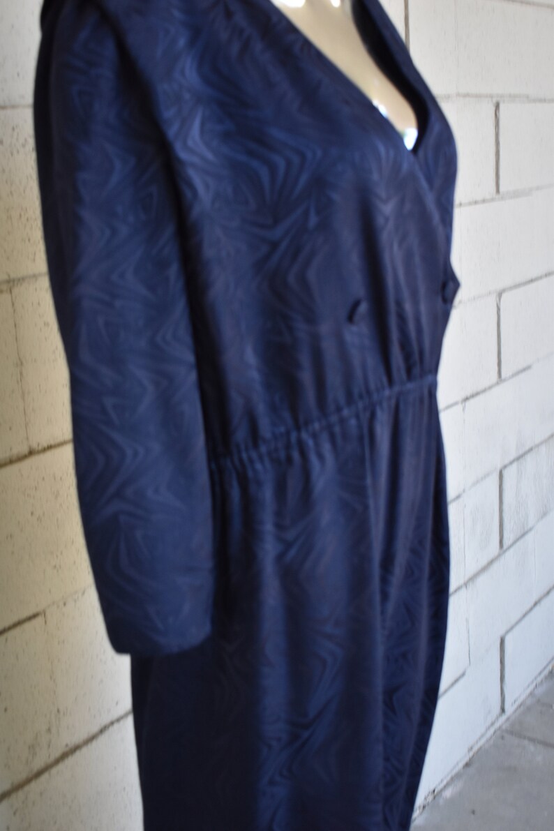 May include: A navy blue dress with a swirling pattern. The dress has a V-neckline and a cinched waist.