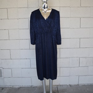 May include: A navy blue dress with a swirling pattern. The dress has a V-neckline and long sleeves. It is fitted through the bodice and flows out to a midi length.
