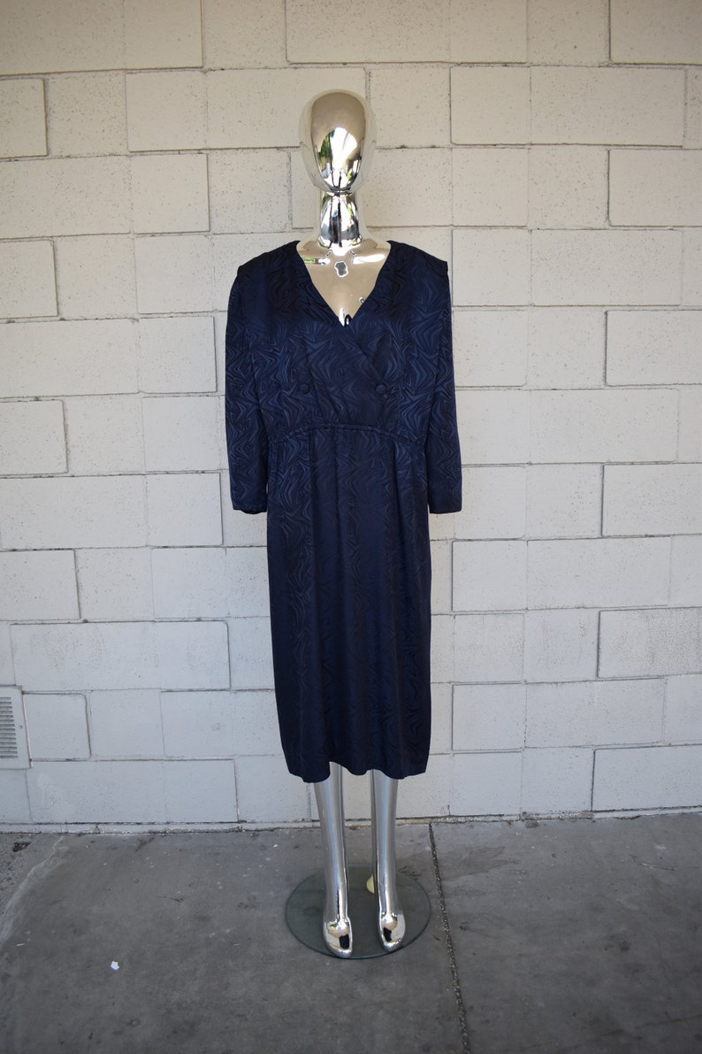 May include: A navy blue dress with a swirling pattern. The dress has a V-neckline and long sleeves. It is fitted through the bodice and flows out to a midi length.