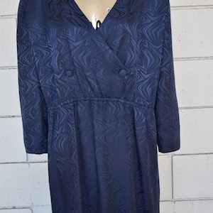 May include: A long-sleeved navy blue dress with a swirling pattern. The dress has a V-neckline and a button closure at the front. The dress has a cinched waist and a flowing skirt.