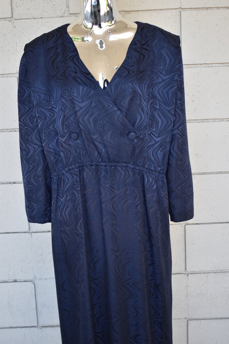 May include: A long-sleeved navy blue dress with a swirling pattern. The dress has a V-neckline and a button closure at the front. The dress has a cinched waist and a flowing skirt.