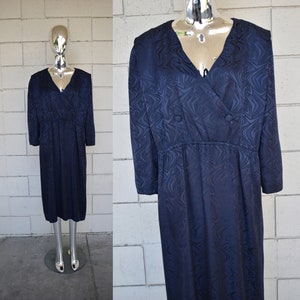 May include: A navy blue dress with a swirling pattern and a v-neckline. The dress has a fitted bodice and a flowing skirt. It features a button closure at the neckline.