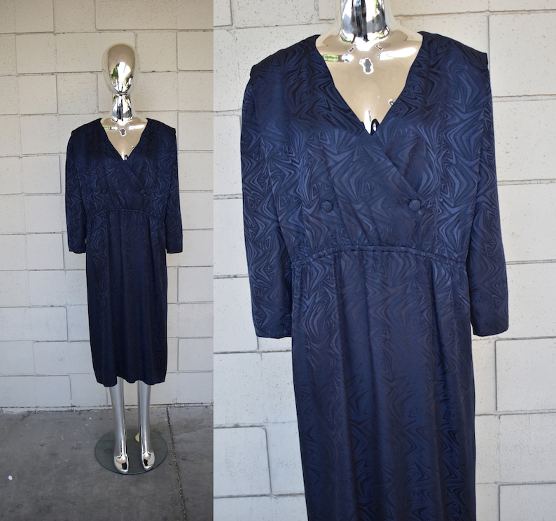 May include: A navy blue dress with a swirling pattern and a v-neckline. The dress has a fitted bodice and a flowing skirt. It features a button closure at the neckline.