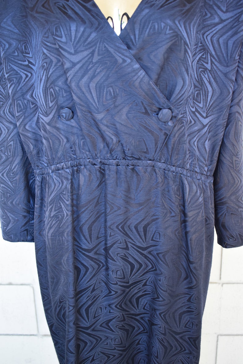 May include: A dark blue wrap dress with a swirling pattern. The dress has a V-neckline and a cinched waist.