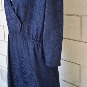 May include: A navy blue dress with a swirling pattern. The dress has a V-neckline, a button closure, and a cinched waist.