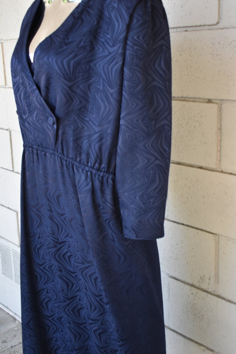May include: A navy blue dress with a swirling pattern. The dress has a V-neckline, a button closure, and a cinched waist.
