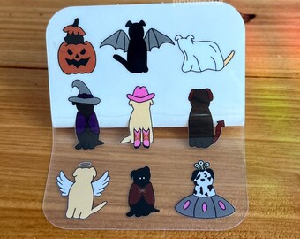 May include: A sheet of stickers featuring various dog breeds dressed in Halloween costumes. The costumes include a pumpkin, a ghost, a witch, a cowboy, a devil, an angel, a vampire, and a space alien.