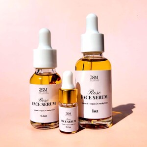 May include: Three glass bottles of Rose Face Serum with white droppers and labels. The bottles are filled with a golden liquid. The labels read "Rose Face Serum" and "Natural | Vegan | Cruelty Free". The sizes are 0.1 oz, 0.5 oz, and 1 oz.