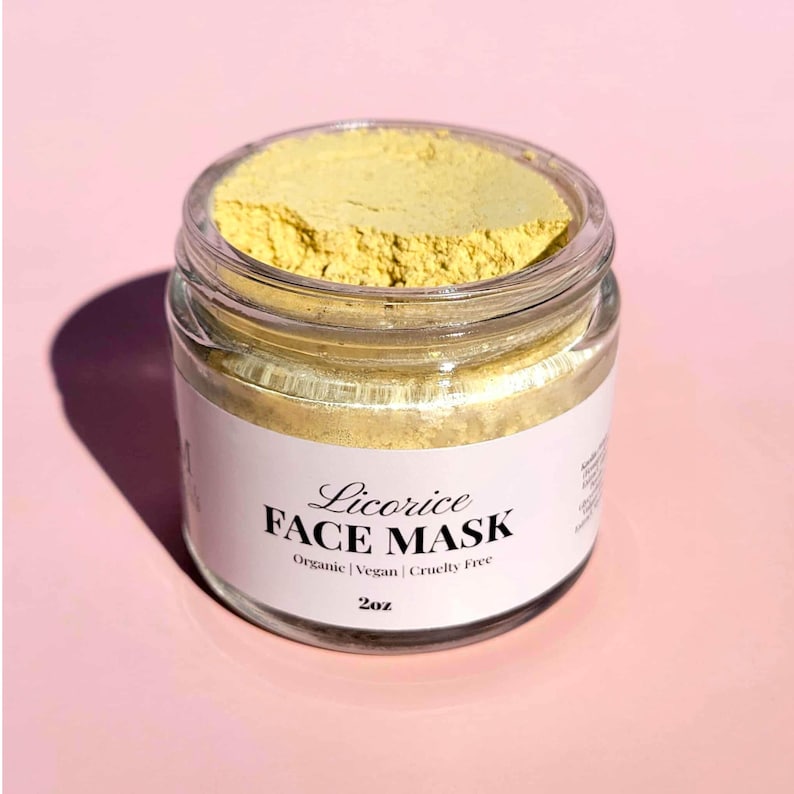 K&ouml;nnte beinhalten: Ein klares Glas mit gelbem Puder, beschriftet mit "Licorice FACE MASK". Das Etikett weist auch "Organic | Vegan | Cruelty Free" und "2oz" aus. Das Glas steht auf einer rosa Oberfl&auml;che.