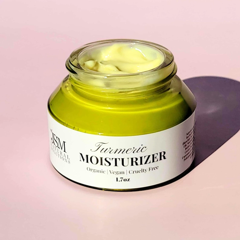 May include: A glass jar of turmeric moisturizer with a yellow cream inside. The jar has a white label with the words "Turmeric Moisturizer" and the text "Organic | Vegan | Cruelty Free". The jar contains 1.7 oz of product.