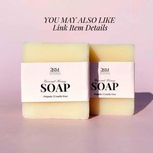 May include: Two bars of Coconut Honey soap with white labels. The labels display the text "JSM NATURAL SOLUTIONS", "Coconut Honey SOAP", and "Organic | Cruelty Free". The soap bars are light yellow and sit on a pink background.