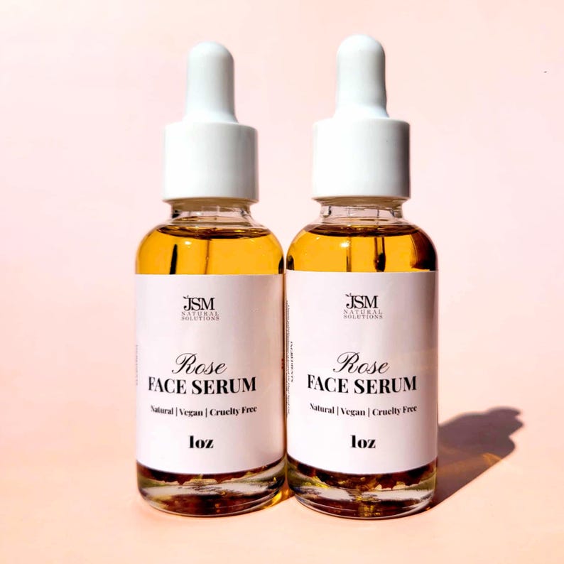 May include: Two glass bottles of Rose Face Serum with white droppers and labels. The labels read "JSM NATURAL SOLUTIONS Rose FACE SERUM Natural | Vegan | Cruelty Free 1oz". The serum is amber-colored.