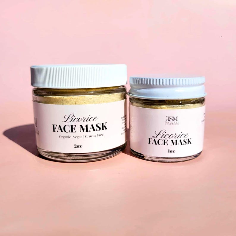 K&ouml;nnte beinhalten: Zwei Gl&auml;ser mit Lakritz-Gesichtsmaske mit wei&szlig;en Deckeln und Etiketten. Auf den Etiketten steht "Licorice Face Mask" und der Text "Organic | Vegan | Cruelty Free". Ein Glas ist mit 2oz beschriftet, das andere mit 1oz.
