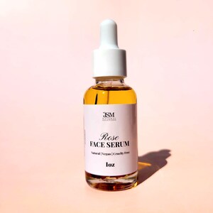 May include: A clear glass bottle of Rose Face Serum with a white dropper top. The label reads "Rose Face Serum, Natural, Vegan, Cruelty Free, 1 oz". The serum is amber-colored.