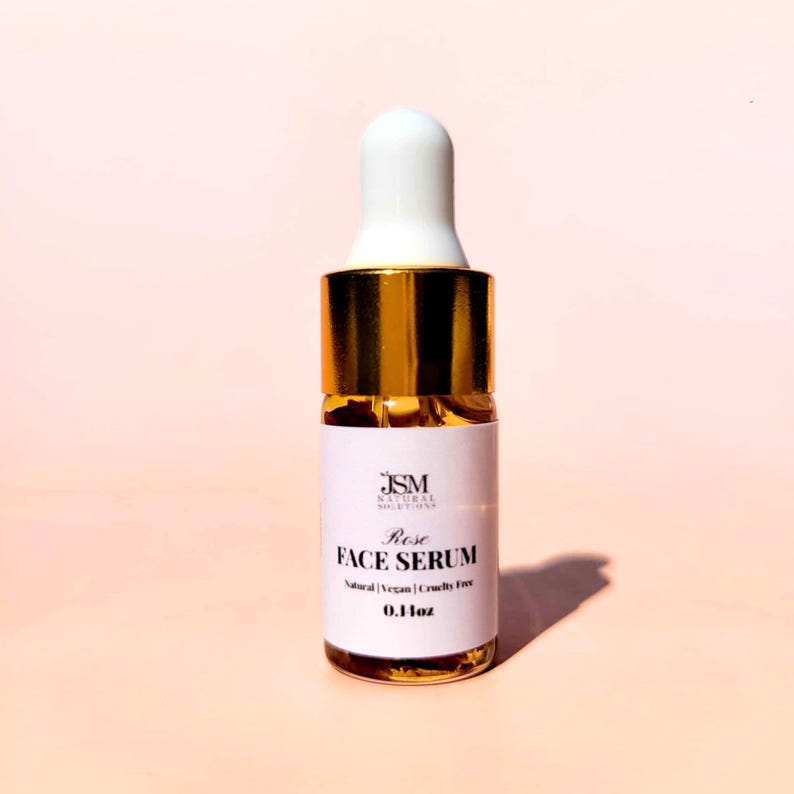 May include: A small glass bottle of Rose Face Serum with a white dropper and gold accents. The label reads "JSM Natural Solutions" and "Rose Face Serum". The bottle contains 0.1 fl oz of serum. The product is natural, vegan, and cruelty-free.
