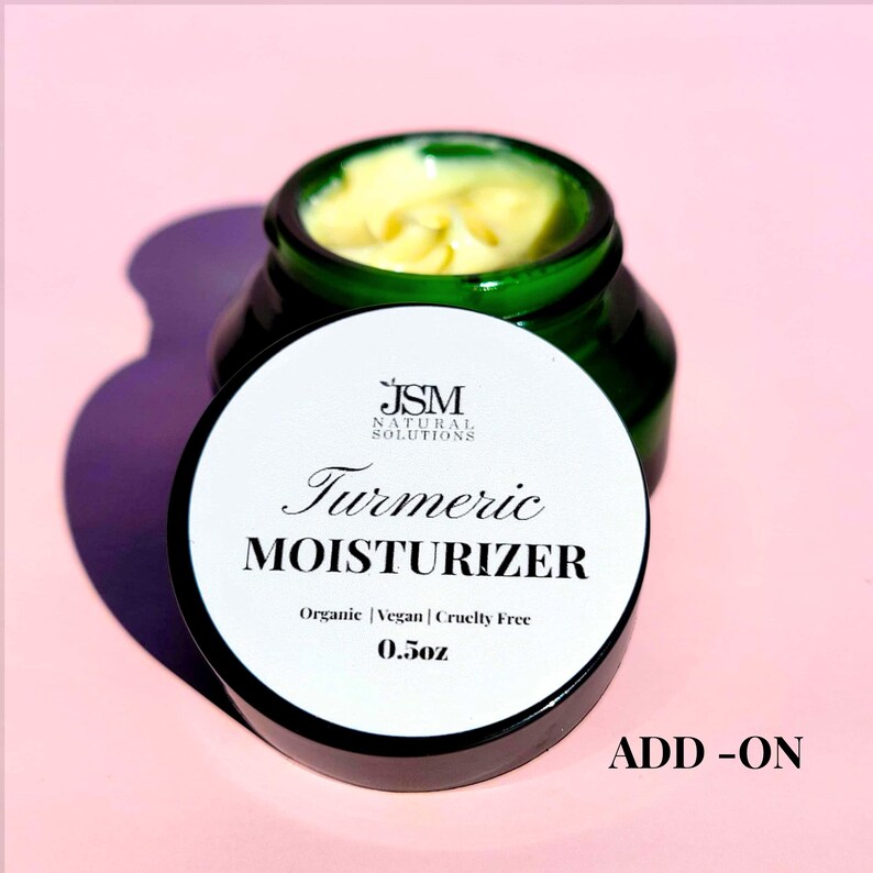 K&ouml;nnte beinhalten: Ein gr&uuml;nes Glas mit Kurkuma-Feuchtigkeitscreme und einem wei&szlig;en Deckel. Der Deckel tr&auml;gt die Aufschrift "Turmeric Moisturizer" und die Produktdetails: "Organic | Vegan | Cruelty Free 14g". Das Glas steht auf einem rosa Hintergrund. Das Wort "ADD-ON" steht unten rechts.