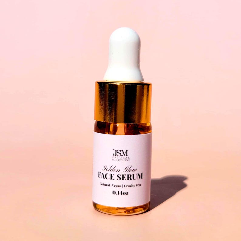 May include: A small glass bottle of Golden Glow Face Serum with a white label and gold accents. The label includes the brand name, product name, and the words "Natural | Vegan | Cruelty Free". The bottle has a white dropper top and contains 0.4 fl oz of serum.