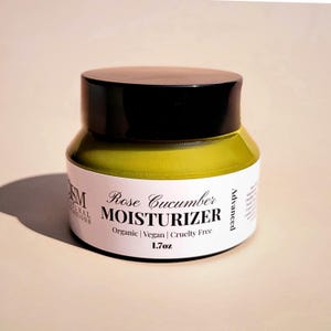 May include: A jar of Rose Cucumber Moisturizer with a black lid and a white label. The label includes the text "Rose Cucumber MOISTURIZER" and "Organic | Vegan | Cruelty Free". The jar contains 48g of product.