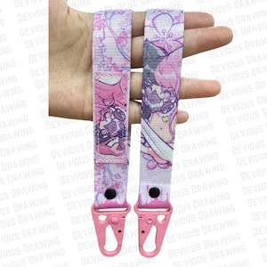 Puede incluir: Dos cordones rosas y blancos con un diseño floral y de personajes de estilo anime. Cada cordón tiene un cierre rosa y un botón negro. Los cordones se muestran sobre un fondo blanco con las palabras "DEVIOUS DRAWING" repetidas.