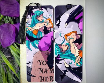 Op de afbeelding: Twee bladwijzers met een cartoon illustratie van een vrouw met turquoise haar, oranje top en paarse outfit. Eén bladwijzer heeft de tekst "YOUR NAME HERE" op een grafsteen. Elke bladwijzer heeft een zwarte kwast.