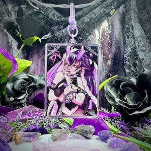 Op de afbeelding: Een rechthoekige, heldere acryl sleutelhanger met een paarse en zwarte anime-stijl illustratie van een personage met hoorns en lang haar. De sleutelhanger heeft een paarse sluiting en is omgeven door paarse en zwarte bloemdecoraties.