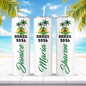 May include: Three white stainless steel tumblers with lids and straws. Each tumbler features a design with palm trees, a sunset, and the text "BRAZIL 2026". The names "Janice", "Maria", and "Sharon" are written in green script.