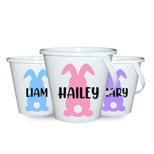 May include: Three white Easter buckets with handles, each featuring a bunny silhouette and a name. The bunny designs are in blue, pink, and purple. The names are Liam, Hailey, and Mary, in black.