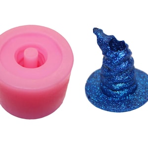 May include: Pink silicone mold for making a blue glitter witch hat. The mold is round with a hole in the center. The hat is a traditional pointed witch hat with a wide brim.