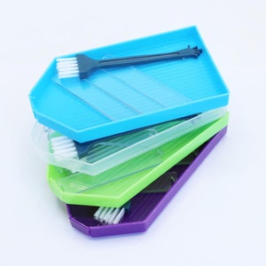 May include: Four stackable plastic trays in blue, clear, green, and purple, with a small blue brush in the top tray.