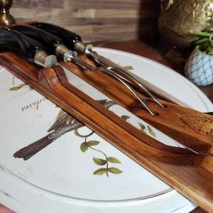 May include: A collection of vintage serving utensils with dark wooden handles and stainless steel blades. The utensils are displayed on a white, round tray featuring a bird and botanical design. The handles are black and silver.