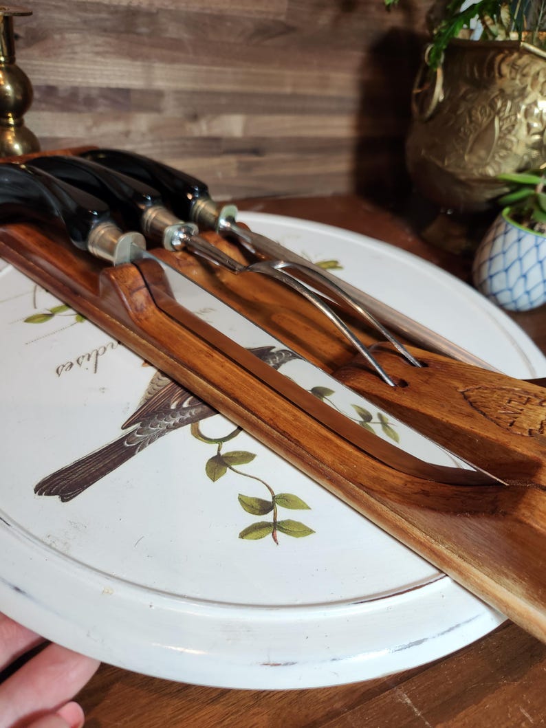 May include: A collection of vintage serving utensils with dark wooden handles and stainless steel blades. The utensils are displayed on a white, round tray featuring a bird and botanical design. The handles are black and silver.