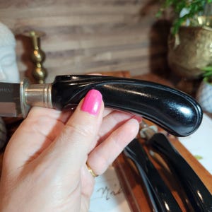 May include: A set of black-handled knives with silver bolsters, presented on a wooden board. The handles have a glossy finish. The knives are likely for a dining setting.