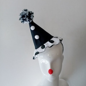 K&ouml;nnte beinhalten: Ein schwarz-wei&szlig;er Polka-Dot-Clownshut mit einem wei&szlig;en Bommel oben. Der Hut sitzt auf einem wei&szlig;en Mannequin-Kopf.
