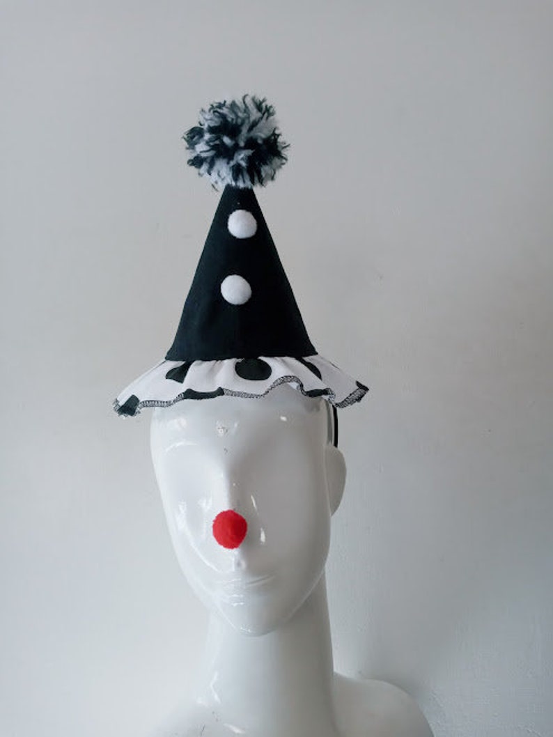 K&ouml;nnte beinhalten: Ein schwarz-wei&szlig;er Clownshut mit einem wei&szlig;en Bommel oben. Der Hut hat einen schwarz-wei&szlig;en Tupfenrand und eine rote Filznase.