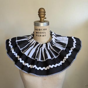 May include: A black and white ruffled collar with a striped pattern, displayed on a mannequin. The collar has a scalloped edge and is made of fabric. The mannequin has the text "MODERN MODEL FORMS" printed on it.