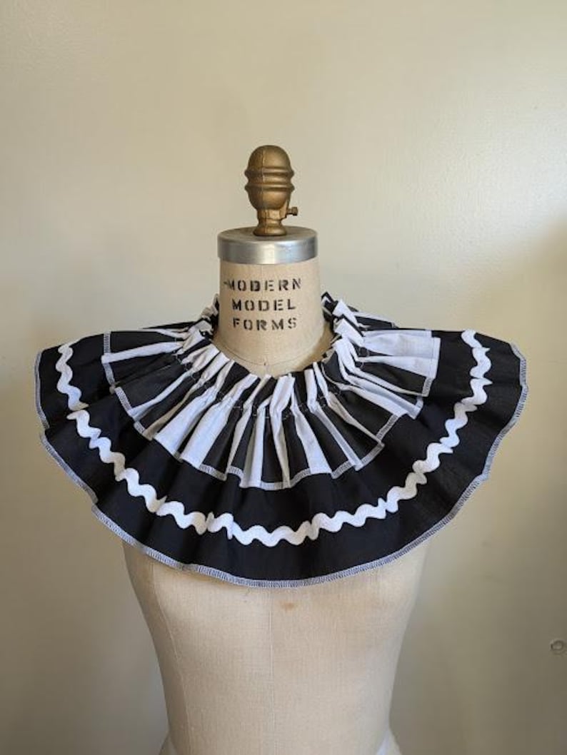May include: A black and white ruffled collar with a striped pattern, displayed on a mannequin. The collar has a scalloped edge and is made of fabric. The mannequin has the text "MODERN MODEL FORMS" printed on it.