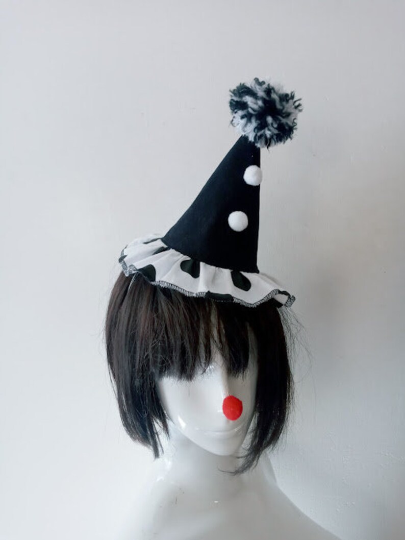K&ouml;nnte beinhalten: Ein schwarz-wei&szlig;er Clownshut mit einem wei&szlig;en Bommel oben. Der Hut hat wei&szlig;e Punkte und einen schwarz-wei&szlig;en Besatz.