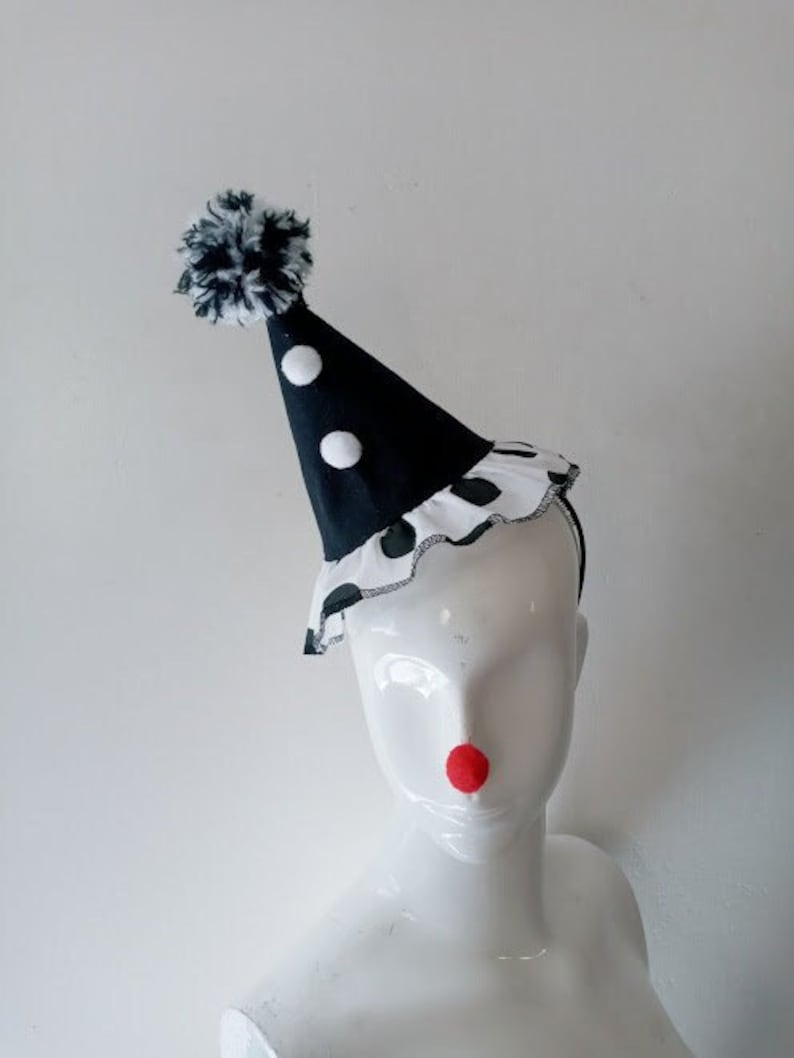K&ouml;nnte beinhalten: Ein schwarz-wei&szlig;er Polka-Dot-Clownshut mit einem wei&szlig;en Bommel oben. Der Hut sitzt auf einem wei&szlig;en Mannequin-Kopf.