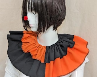 May include: A black and orange ruffled clown collar. The collar is two-toned, with alternating black and orange sections. A red clown nose is visible on the mannequin's face. The mannequin is wearing a white t-shirt.