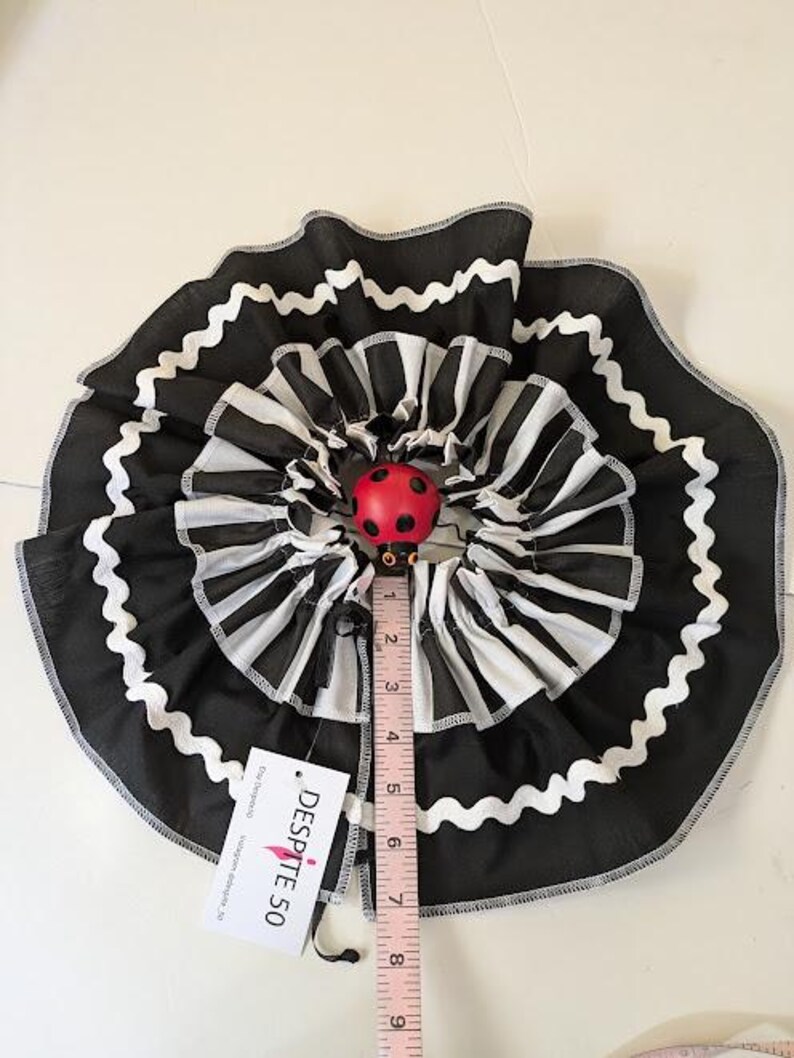 May include: A black and white striped ruffled skirt with a red ladybug accent. The skirt is approximately 5 inches in diameter. The skirt has a white zigzag trim and a tag that says "DESPITE 50".