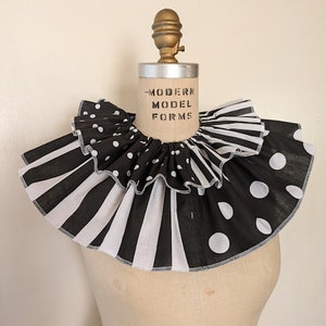 May include: A black and white ruffled collar with polka dots and stripes. The collar is on a dress form with the text "MODERN MODEL FORMS" printed on the front.