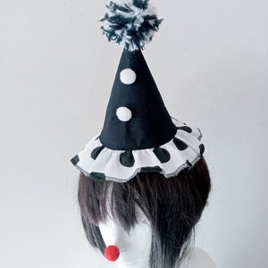 K&ouml;nnte beinhalten: Ein schwarz-wei&szlig;er Clownshut mit einem wei&szlig;en Bommel oben. Der Hut hat einen wei&szlig;en R&uuml;schenbesatz mit schwarzen Punkten am unteren Rand.