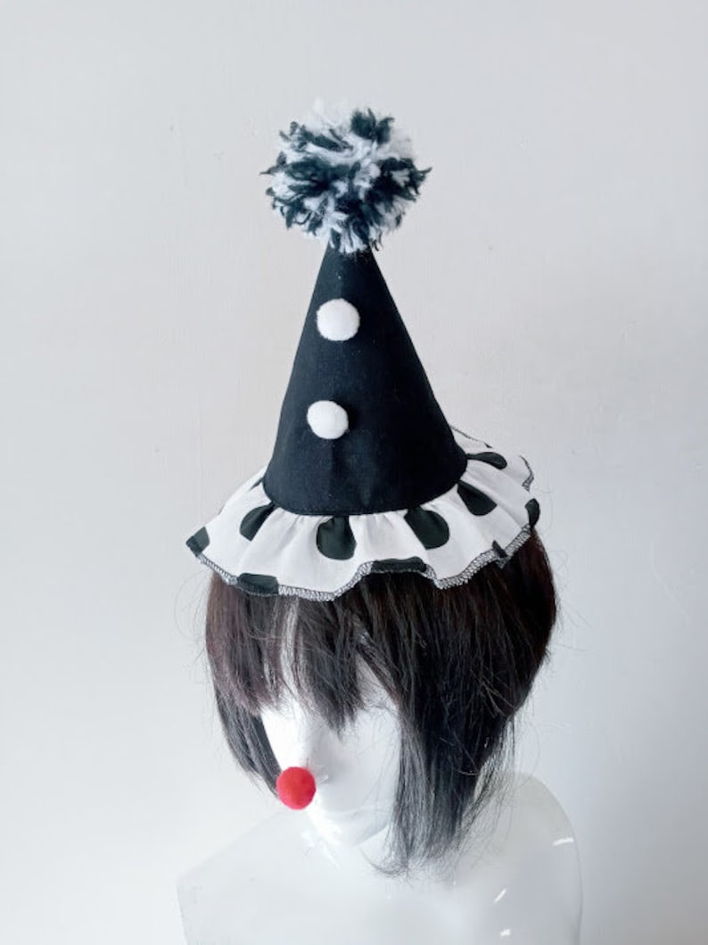 K&ouml;nnte beinhalten: Ein schwarz-wei&szlig;er Clownshut mit einem wei&szlig;en Bommel oben. Der Hut hat einen wei&szlig;en R&uuml;schenbesatz mit schwarzen Punkten am unteren Rand.