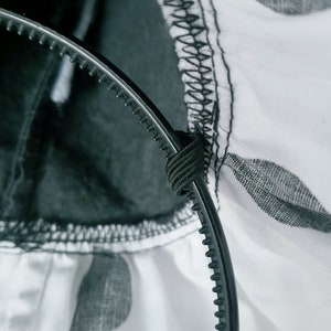 K&ouml;nnte beinhalten: Ein schwarzes Stirnband mit strukturierter Oberfl&auml;che und einem wei&szlig;en Hintergrund aus gepunktetem Stoff.