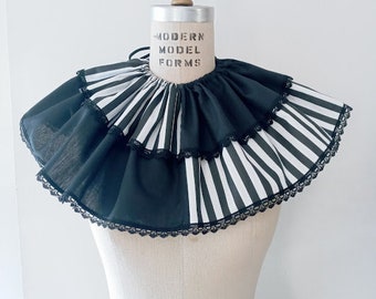 May include: A black and white striped ruffled collar with black lace trim. The collar is on a white dress form with the text "MODERN MODEL FORMS" printed on the front.