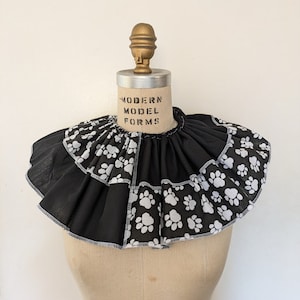 May include: A black and white ruffled collar with a paw print design. The collar is on a dress form with the text "MODERN MODEL FORMS" on the bust.