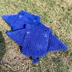 Op de afbeelding: Drie blauwe gehaakte roggen knuffels met witte geborduurde ogen. De knuffels zijn gestapeld met de grootste onderaan.
