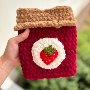 Peut inclure: Étui en crochet rouge fait à la main avec un motif de fraise. L'étui présente un cercle blanc avec une fraise rouge et des feuilles vertes au centre. Le bord supérieur est de couleur marron texturé.