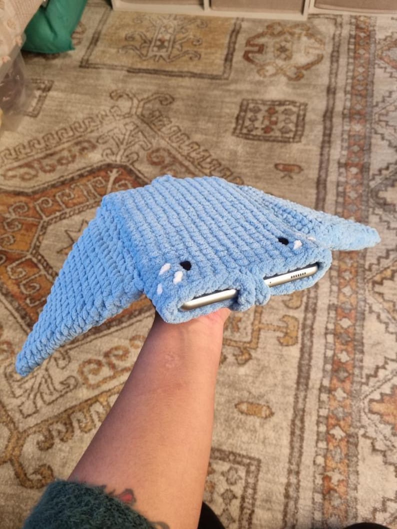 Op de afbeelding: Een blauwe gehaakte tablet hoes in de vorm van een mantarog. De hoes heeft twee witte ogen en een witte mond.